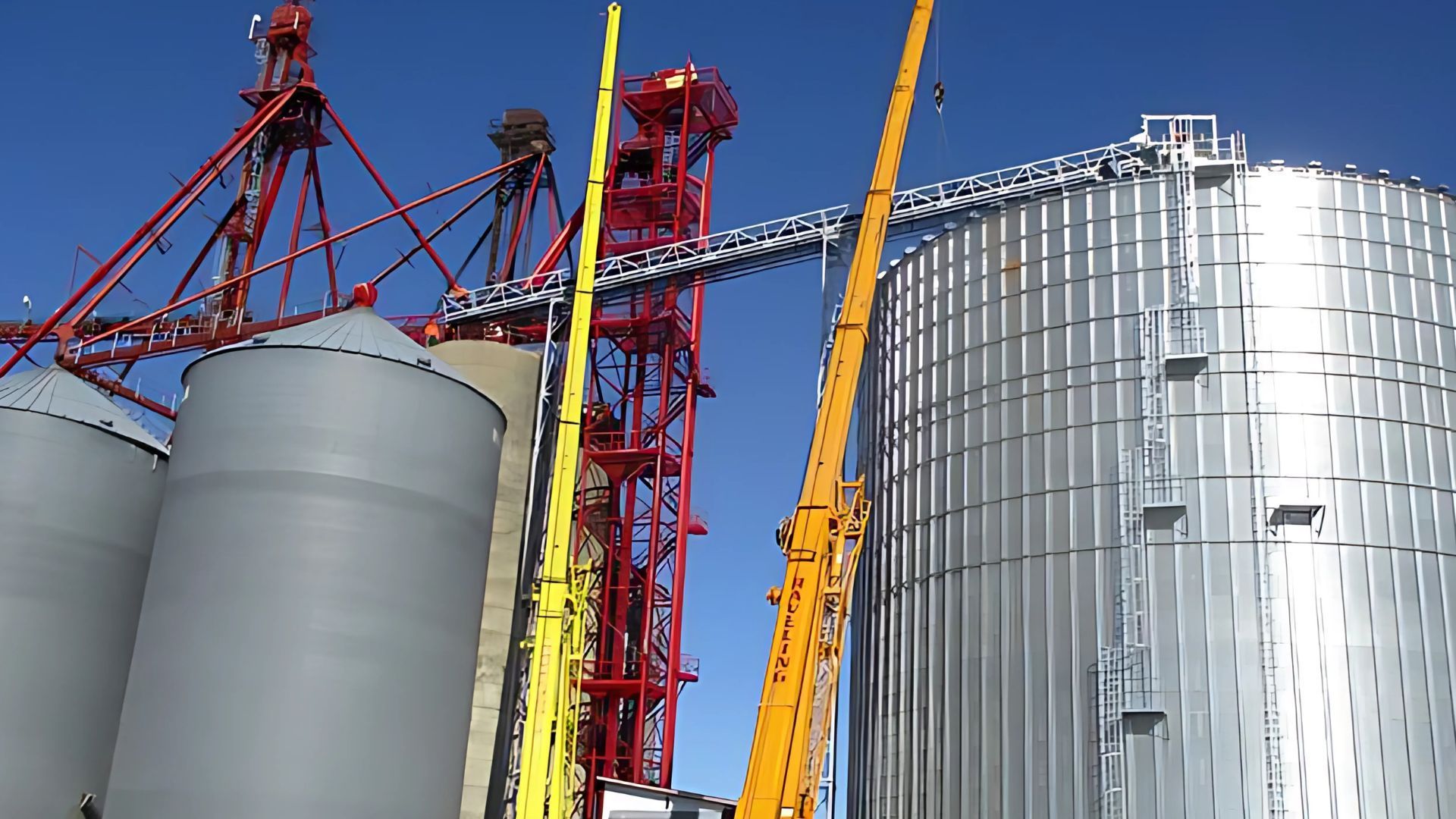 A large silo with a yellow crane in front of it