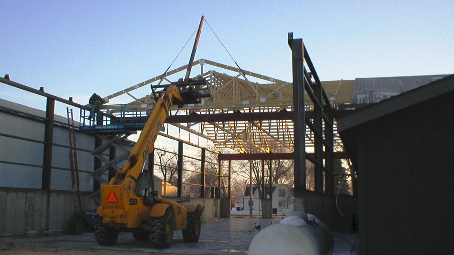 A yellow forklift is lifting a metal structure in a building under construction