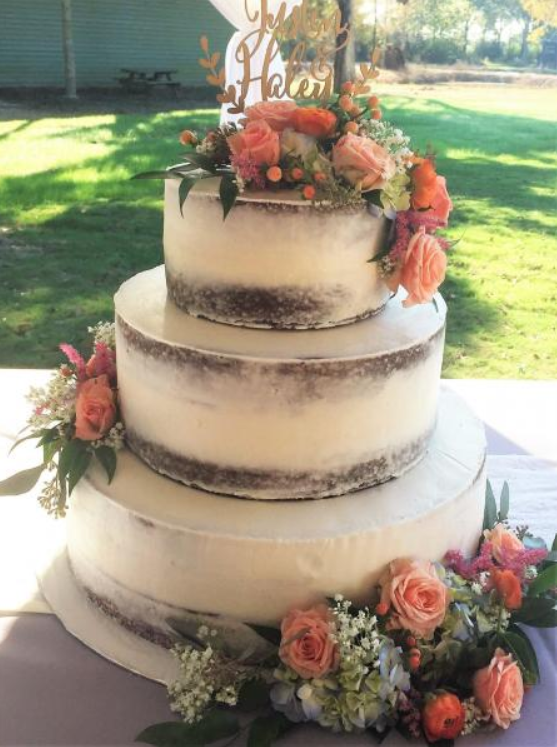 Three-tier wedding cake with peach and coral flowers on a table outdoors