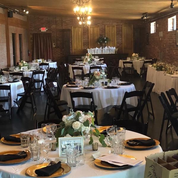 Elegant banquet hall with round tables, white tablecloths, black chairs, and floral centerpieces under warm lights