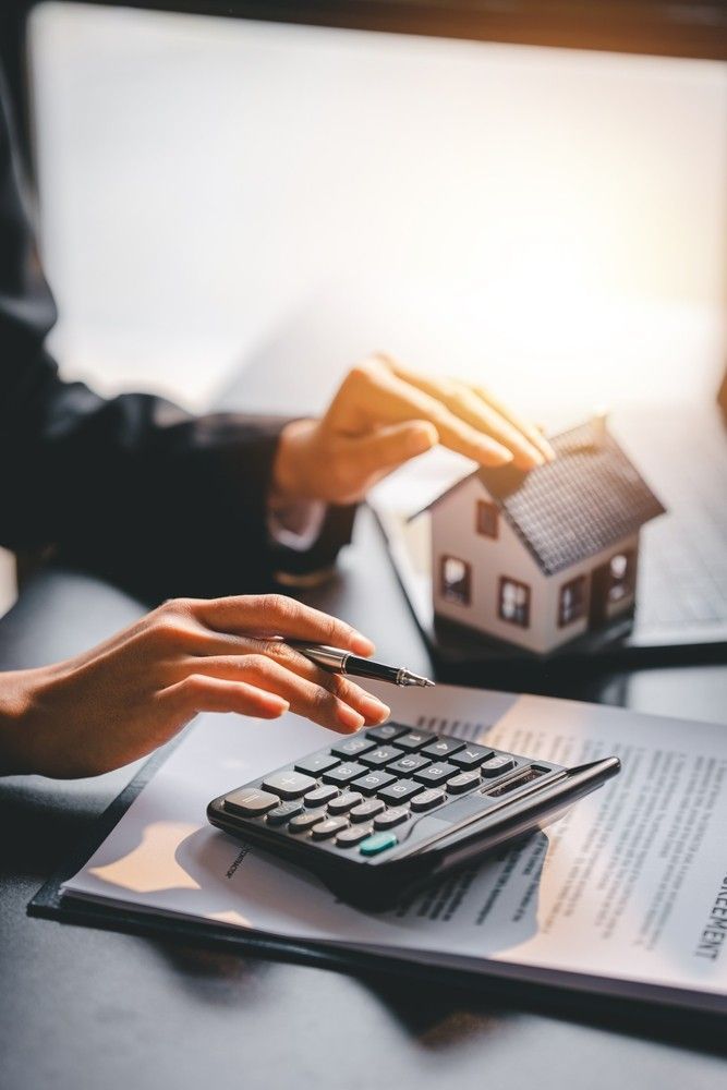 A Person is Using a Calculator With a Model House in the Background — Loan Select Tablelands in Atherton, QLD