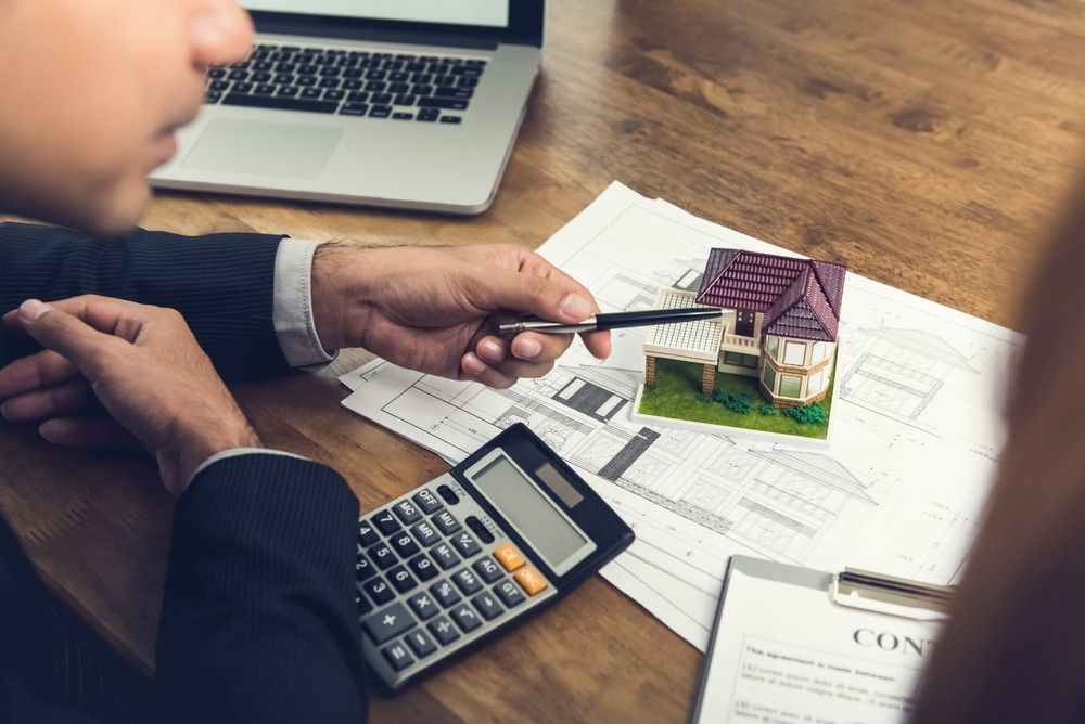 A Man is Sitting at a Table With a Calculator and a Model House — Loan Select Tablelands in Atherton, QLD