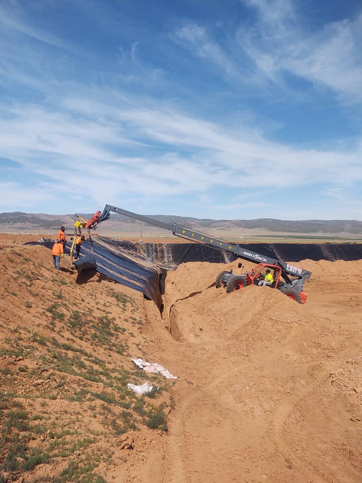 Workers using construction equipment to install black liner on hill