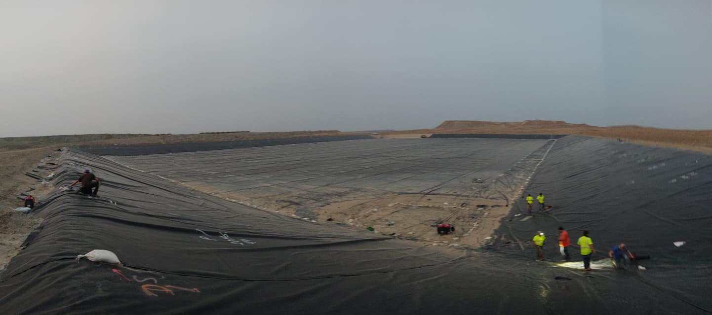Large resevoir-sized are covered with black lining.  Five workers installing in work apparel