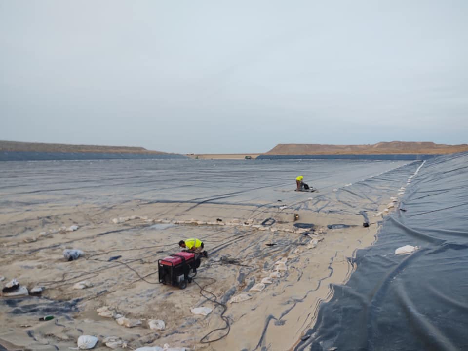 Large flat surface surrounded by ridges.  Worker installing a very large area of liner
