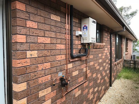 A Brick House with A Copper Pipe Attached to The Side of It — Lakesway Plumbing and Gas in Forster, NSW