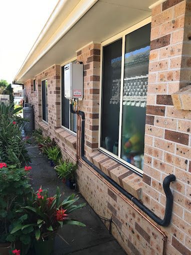 A Brick House with A Hose Attached to The Side of It — Lakesway Plumbing and Gas in Tuncurry, NSW