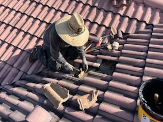 A man wearing a hat is working on a tiled roof.
