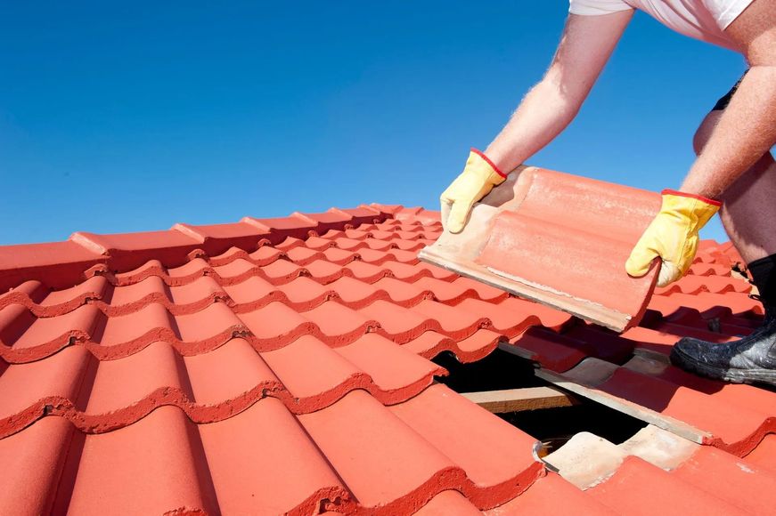 A man wearing yellow gloves is laying a red tile on a roof.