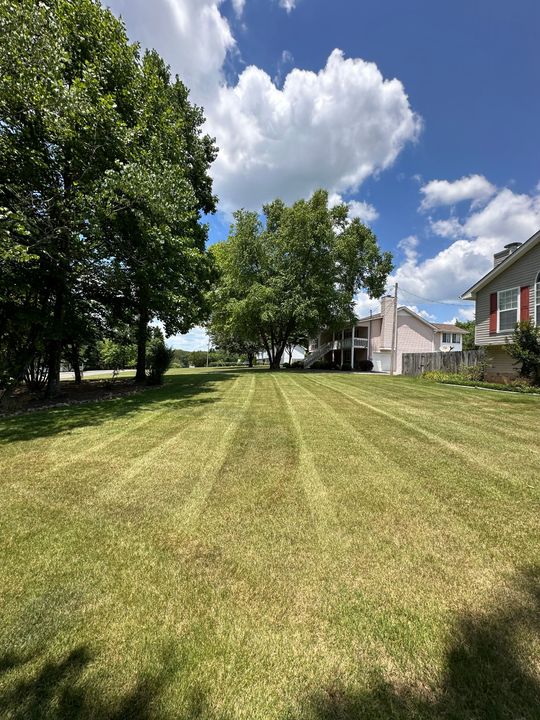 A lush green lawn is being mowed in front of a house on a sunny day.