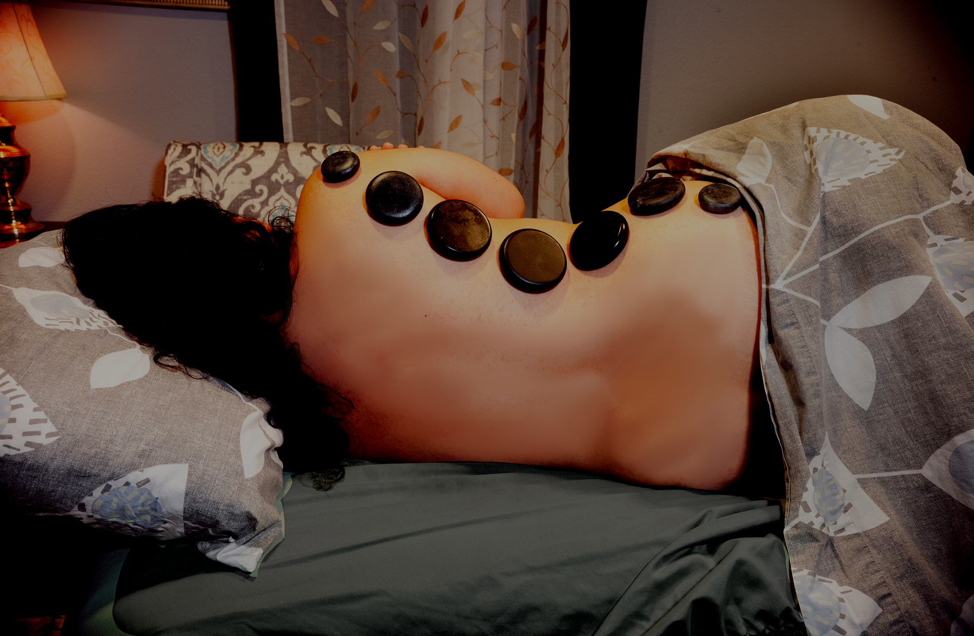 A woman is laying on a bed with rocks on her back.