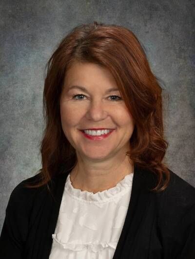 A woman with long blonde hair is smiling in front of a purple background
