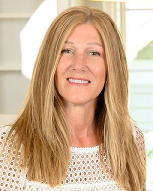 A woman with long blonde hair is wearing a white shirt and smiling.