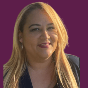 A woman with long blonde hair is smiling in front of a purple background