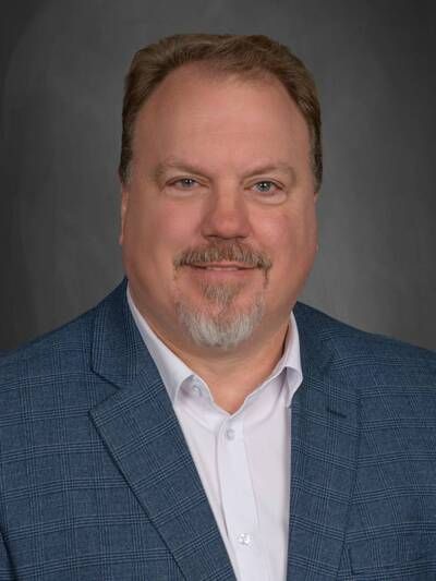 A man in a blue sweater is smiling in front of a brick wall.