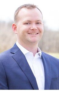 A man in a blue suit and white shirt is smiling for the camera.