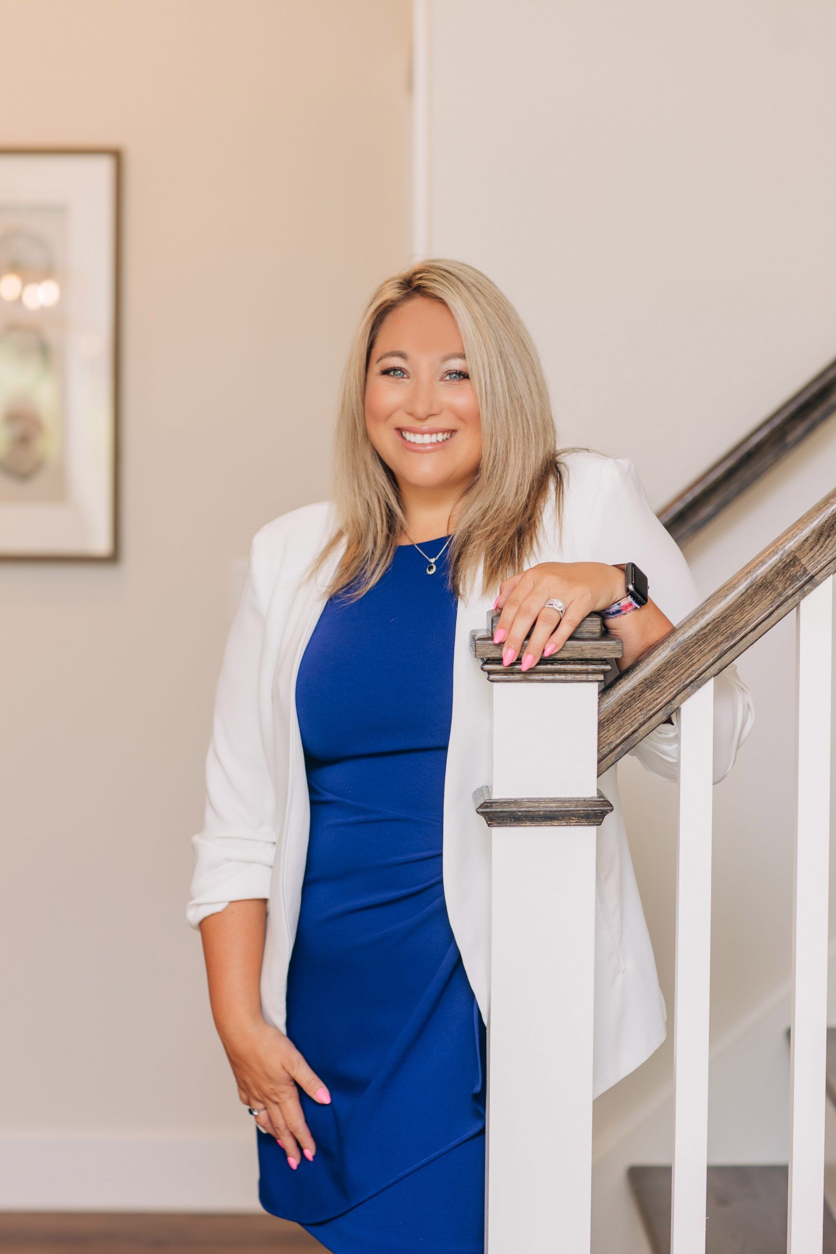 A woman in a blue dress and white jacket is leaning on a railing.