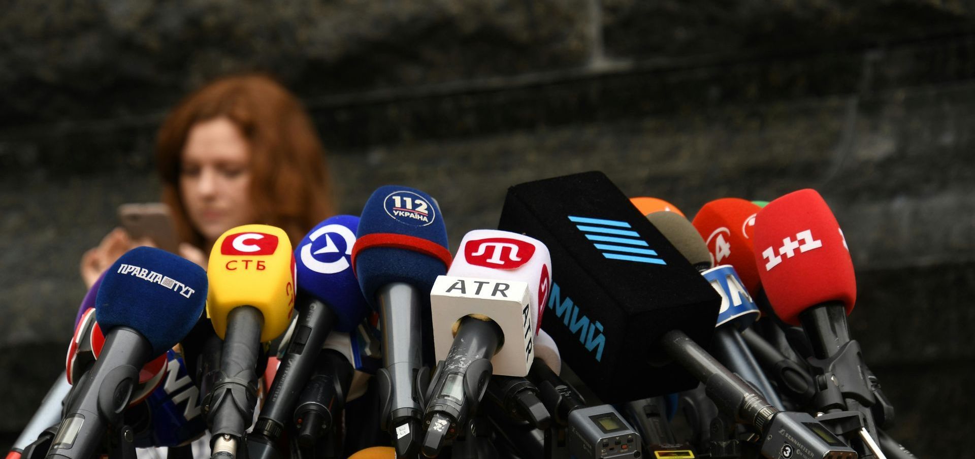 A woman looks at her phone in front of a bunch of microphones one of which says air