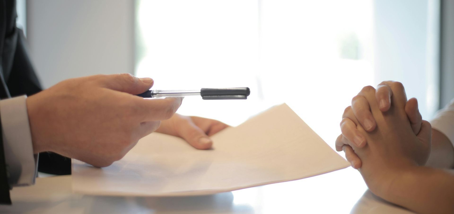 A man is holding a pen over a piece of paper while a woman holds her hands together.