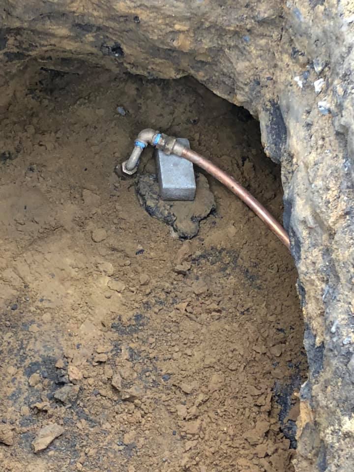 A copper pipe is laying in the dirt in a hole.