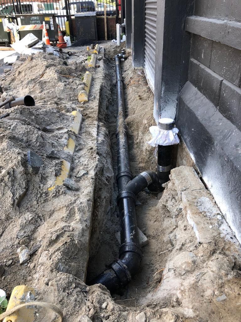 A pipe is being installed in the dirt next to a building.