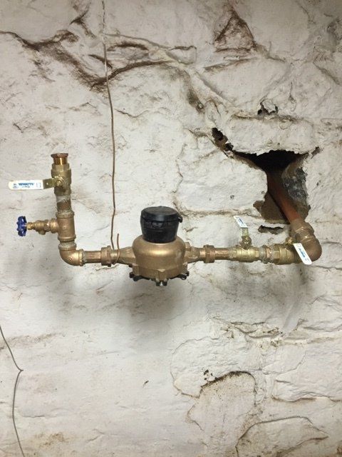 A water meter is attached to a wall with a hole in it