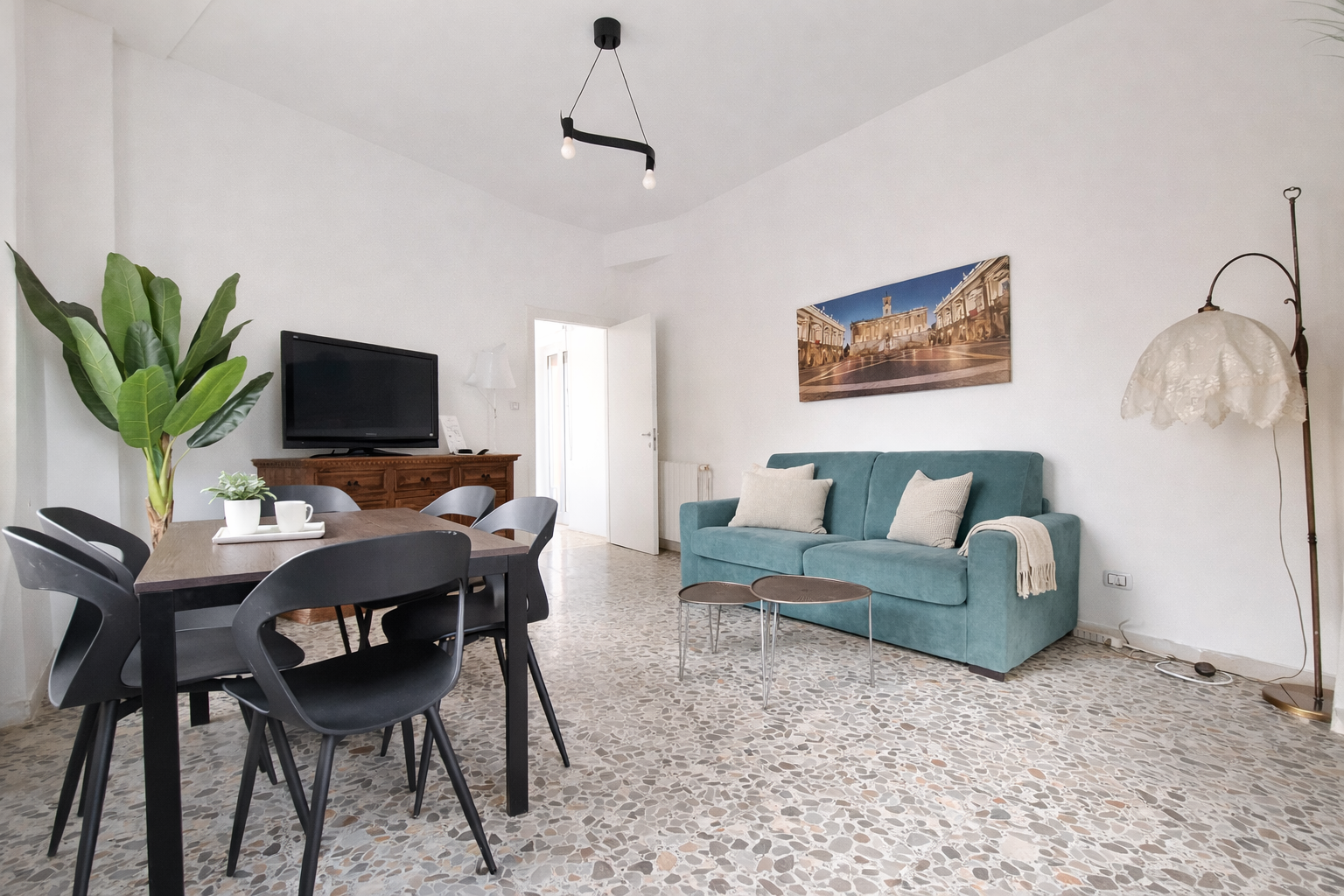 Soggiorno con tavolo da pranzo, divano blu e opere d'arte sulle pareti bianche.