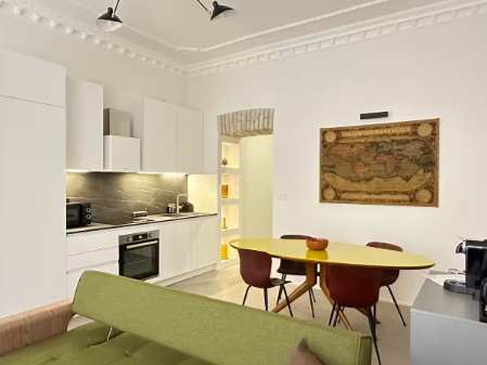 Soggiorno con tavolo da pranzo, divano blu e opere d'arte sulle pareti bianche.