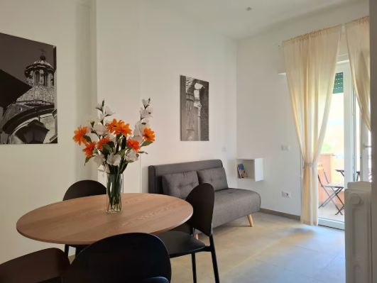 Zona pranzo con tavolo, sedie, divano, fiori, opere d'arte e accesso al balcone.