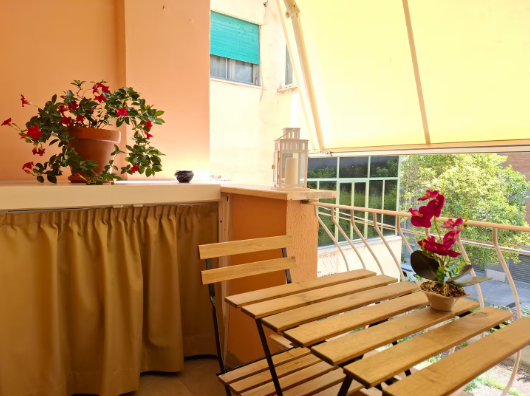 Balcone con tavolo, sedie, piante in vaso e tenda da sole gialla.