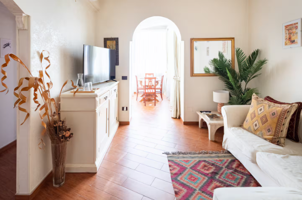 Luminoso soggiorno con divano bianco, pavimenti in cotto e arco che conduce alla zona pranzo.