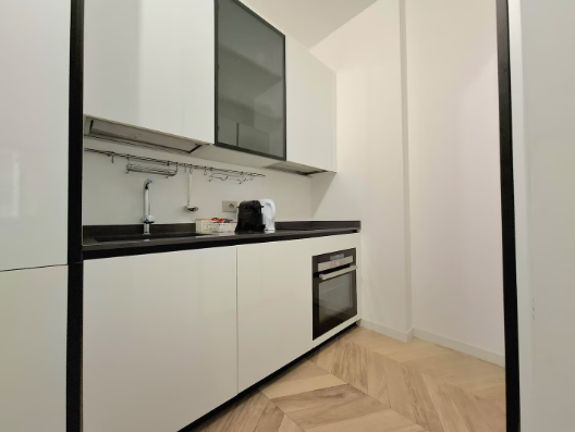 Moderna cucina bianca con ripiani e forno neri, pavimento in legno chiaro.