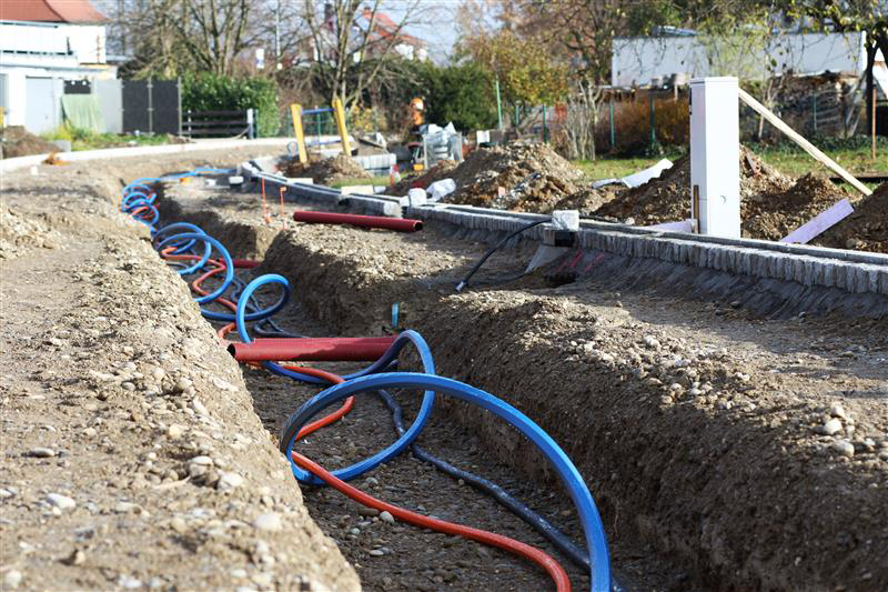 Trenches with red and blue pipes, construction site.