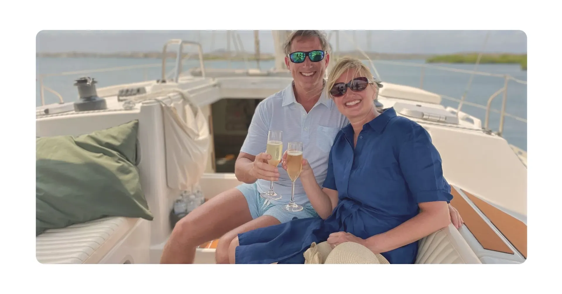 Couple toasting champagne on a private boat, sunny day, blue water.