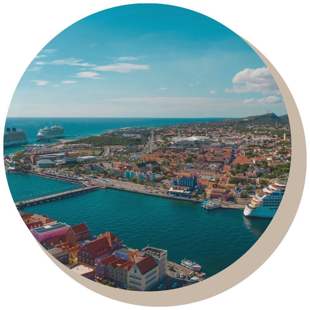 Coastal city with colorful buildings, bridge, cruise ships, and blue water under a clear sky.