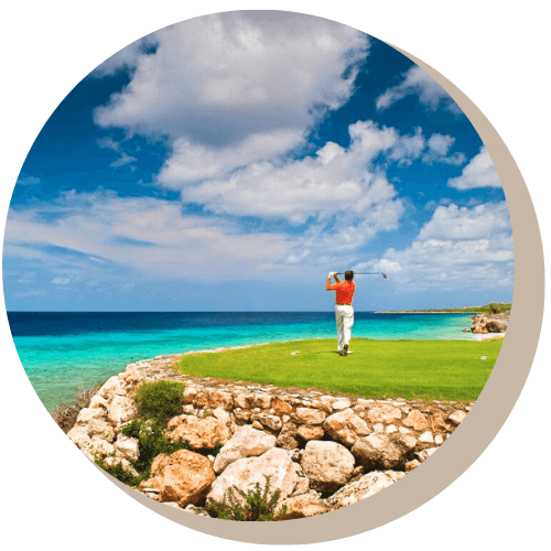 Men teeing off on Old Quarry Course, green, ocean view, bright blue sky with clouds.