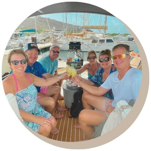 Four people on a sailboat, enjoying drinks with a coastal mountain backdrop.