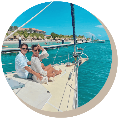 Couple on sailboat, blue water, sunny day. Coastline in background.