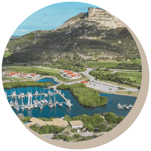 Marina with boats, buildings, and a mountain in the background under a blue sky.
