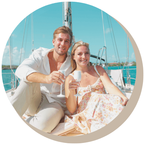Couple on sailboat, toasting with champagne; blue sea and sky in background.