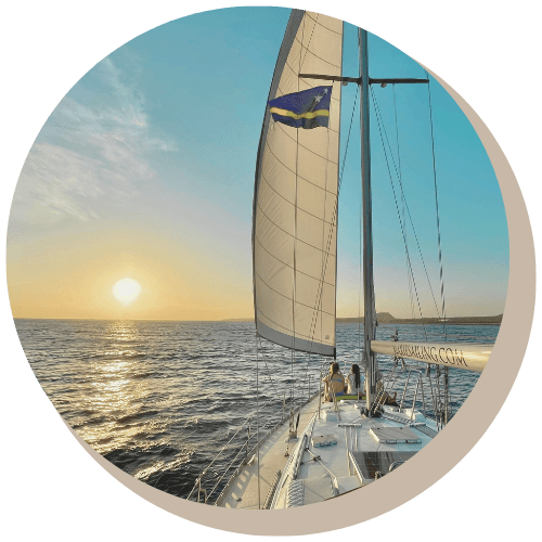 Sailboat on the ocean at sunset, with a couple sitting on the boat.