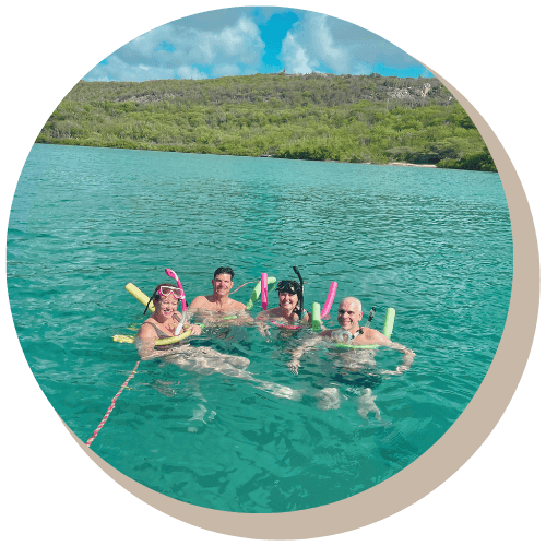 Sailboat in turquoise water near a green-covered shoreline under a blue sky.