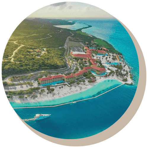 Aerial view of a coastal resort with buildings, a white beach, and turquoise ocean.