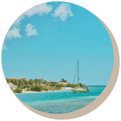 Turquoise ocean with a green sailboat, shoreline, and blue sky with clouds.