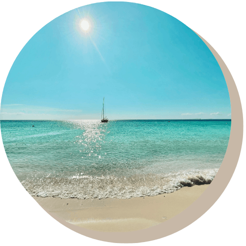 Bright sun over turquoise water, small boat on horizon, sandy beach.