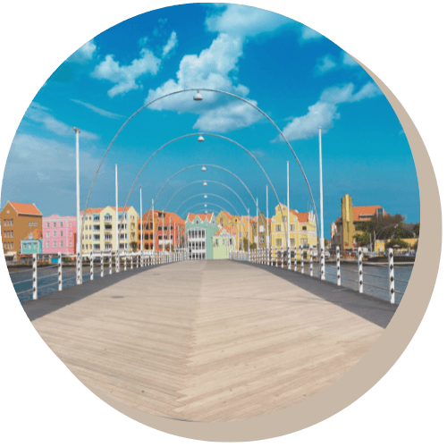 Wooden floating bridge leading to colorful buildings under a blue sky, Curacao.