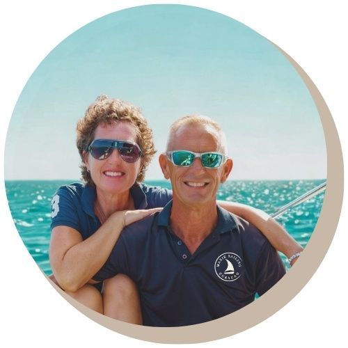 Smiling couple Hilde and Norbert - owners of Maxie Sailing private boat charter Curacao wearing sunglasses outdoors; woman's arm over man's shoulder.