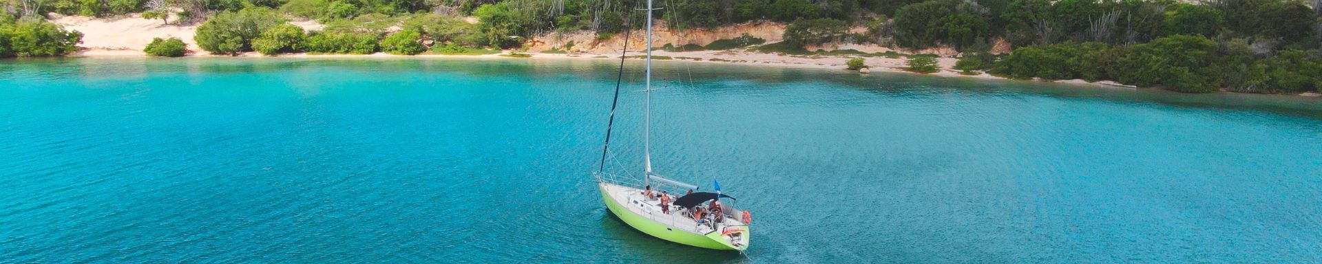 sailing yacht Galaxie floats in turquoise water of Fuik Bay on a private boat tour with Maxie Sailing near a shoreline with mangroves and green flora.