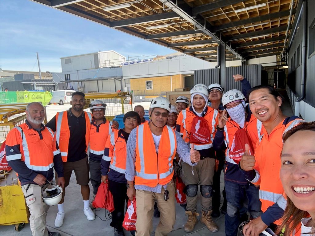Construction crew in orange vests and hard hats, smiling and giving thumbs up.