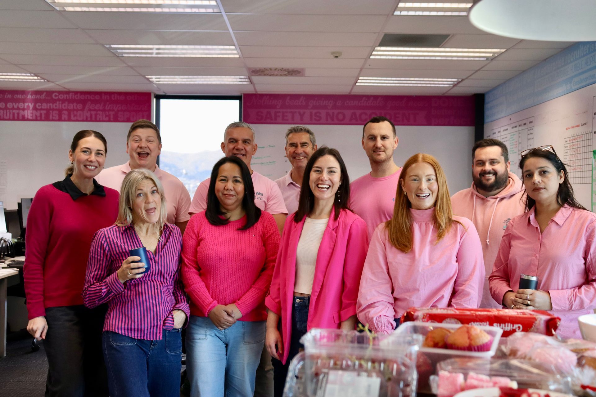 Group of people wearing pink smiling in an office setting.